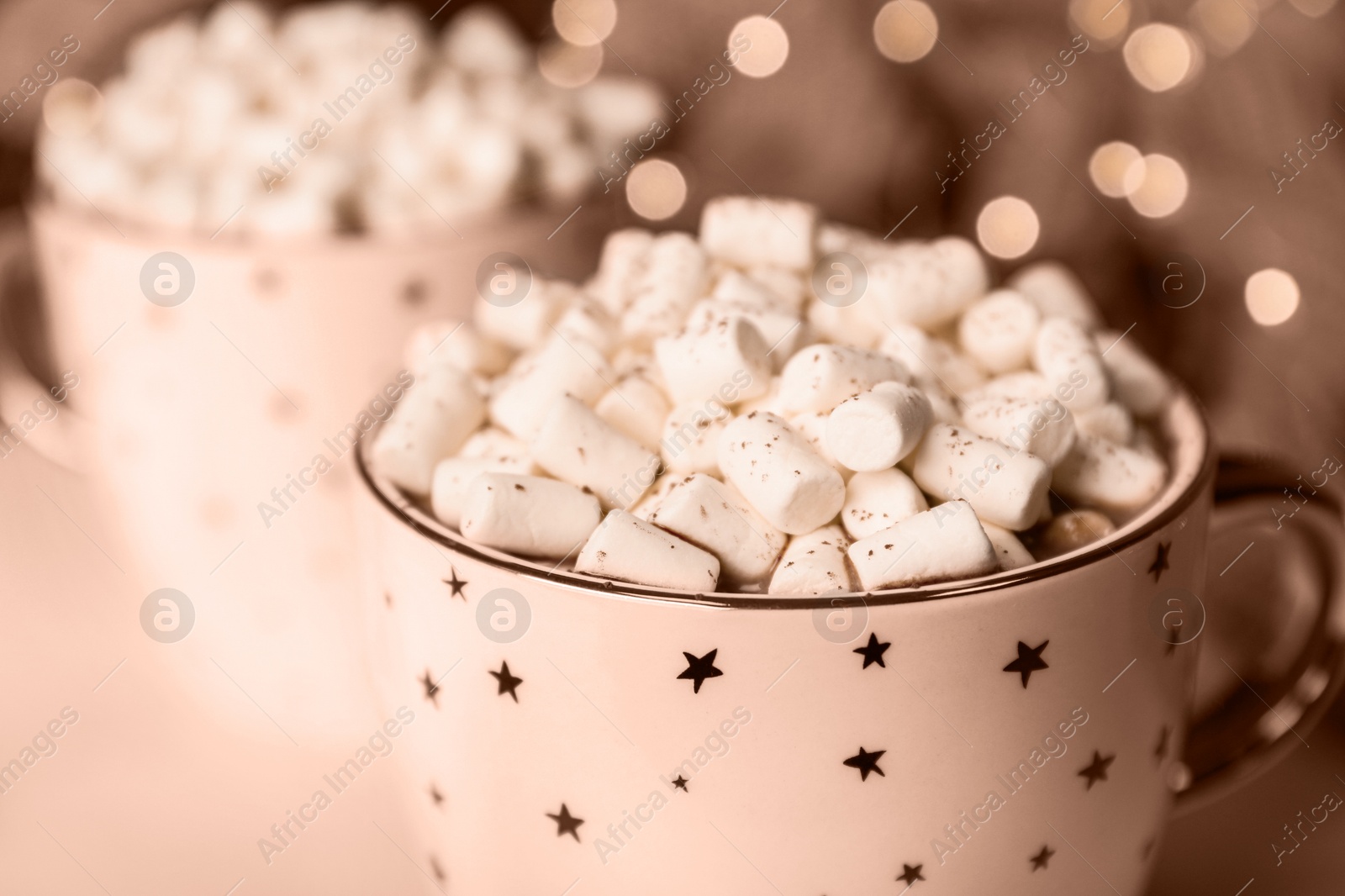 Image of Delicious cocoa drink with marshmallows on table against blurred lights, toned in mocha mousse shade. Trendy color of 2025 year