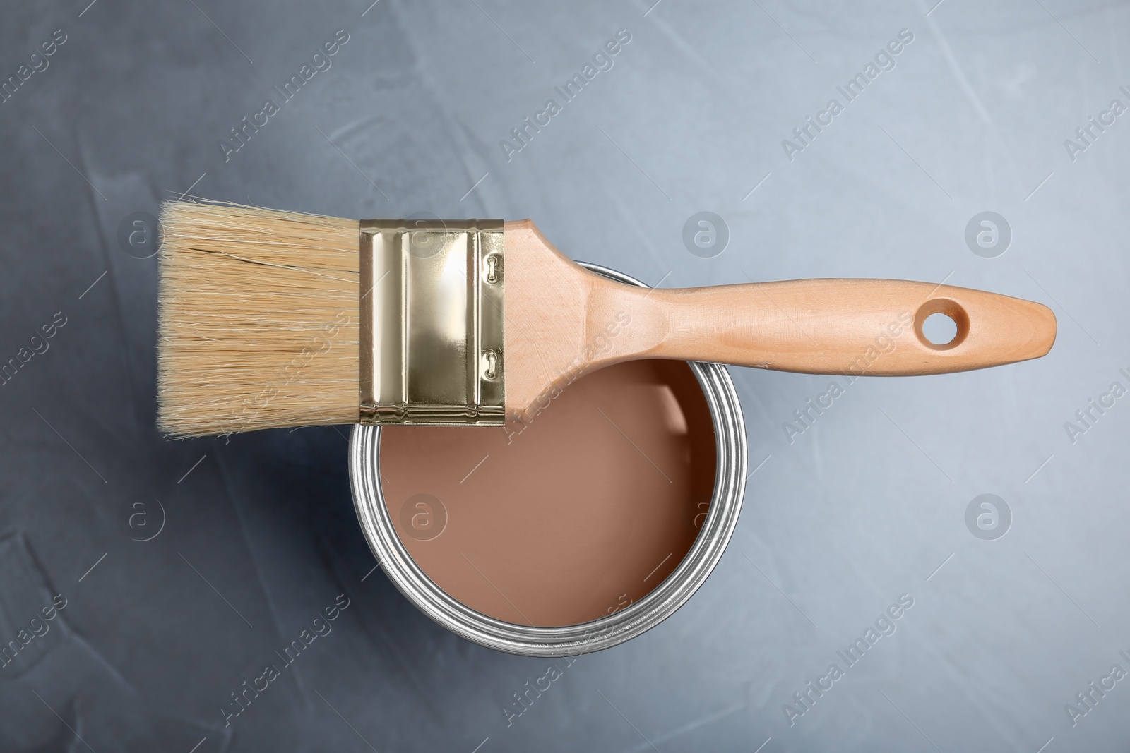 Image of Mocha mousse shade paint in can and brush on grey background, top view. Trendy color of 2025 year