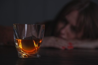 Image of Alcohol addiction. Woman at table, focus on glass of whiskey