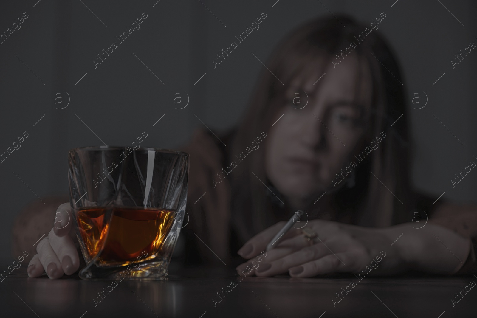 Image of Alcohol addiction. Woman with glass of whiskey and cigarette at table, selective focus