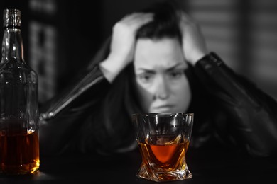 Image of Alcohol addiction. Depressed woman at table, focus on glass of whiskey