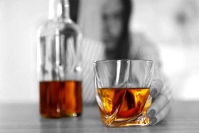 Alcohol addiction. Depressed woman with glass of whiskey and bottle at table, selective focus