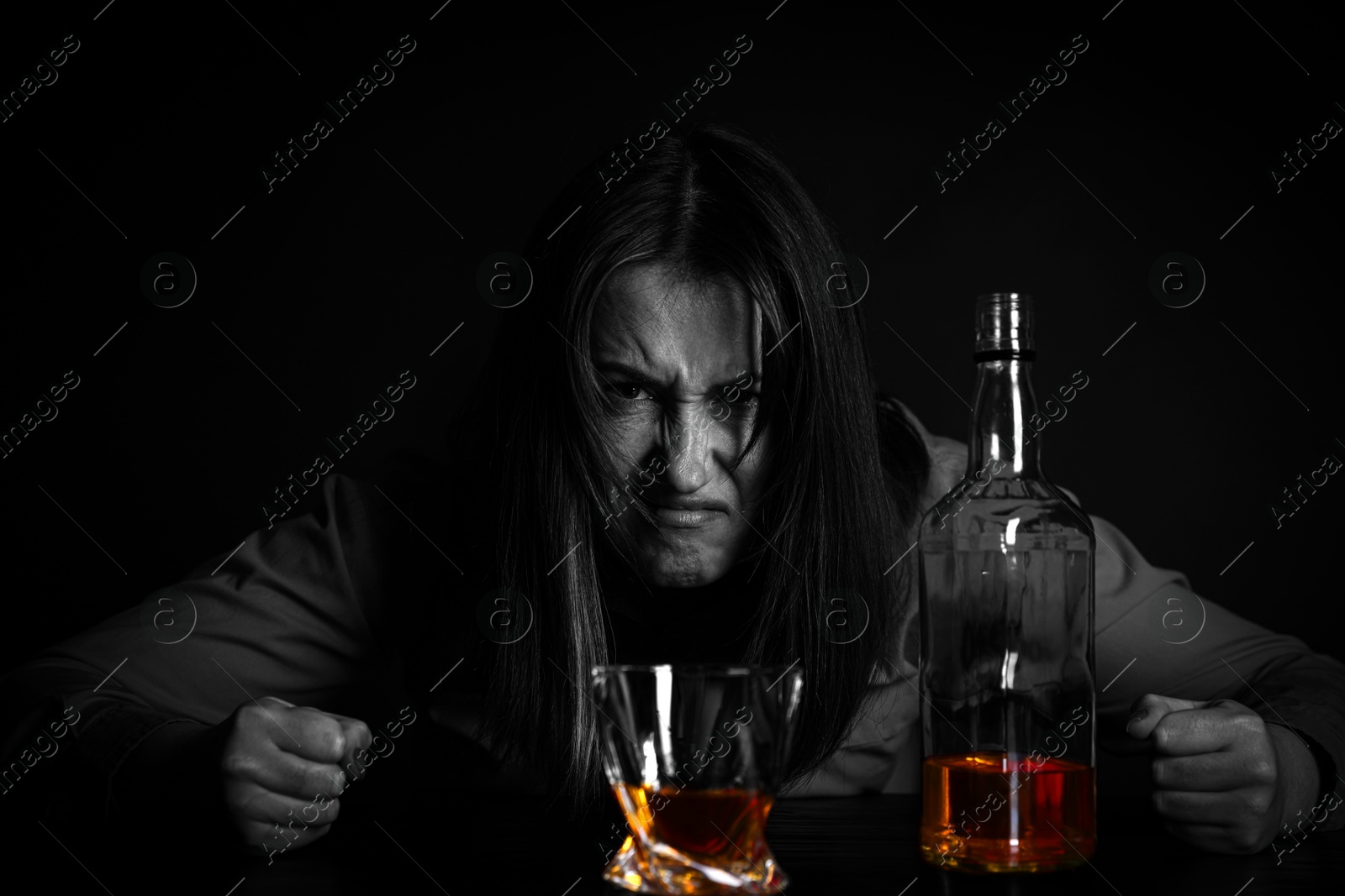 Image of Alcohol addiction. Angry woman with whiskey at table in darkness