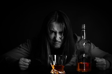 Image of Alcohol addiction. Angry woman with whiskey at table in darkness