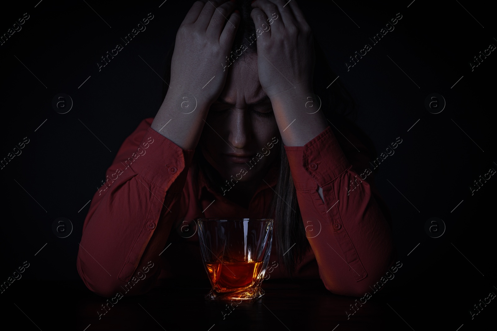 Image of Alcohol addiction. Depressed woman with whiskey at table in darkness