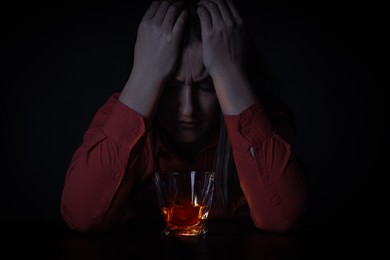 Image of Alcohol addiction. Depressed woman with whiskey at table in darkness