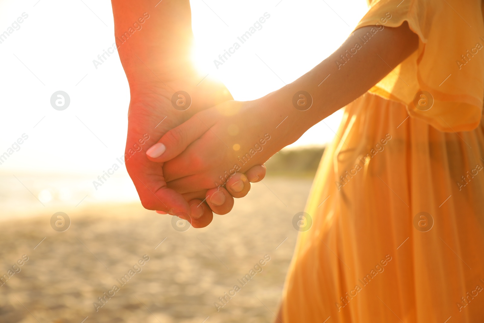 Photo of Lovely couple holding hands on beach at sunset, closeup