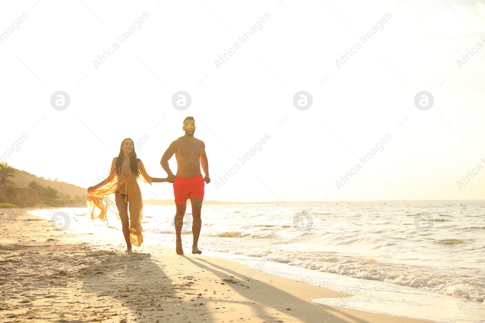 Photo of Happy young couple running together on beach at sunset