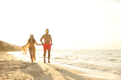 Photo of Happy young couple running together on beach at sunset