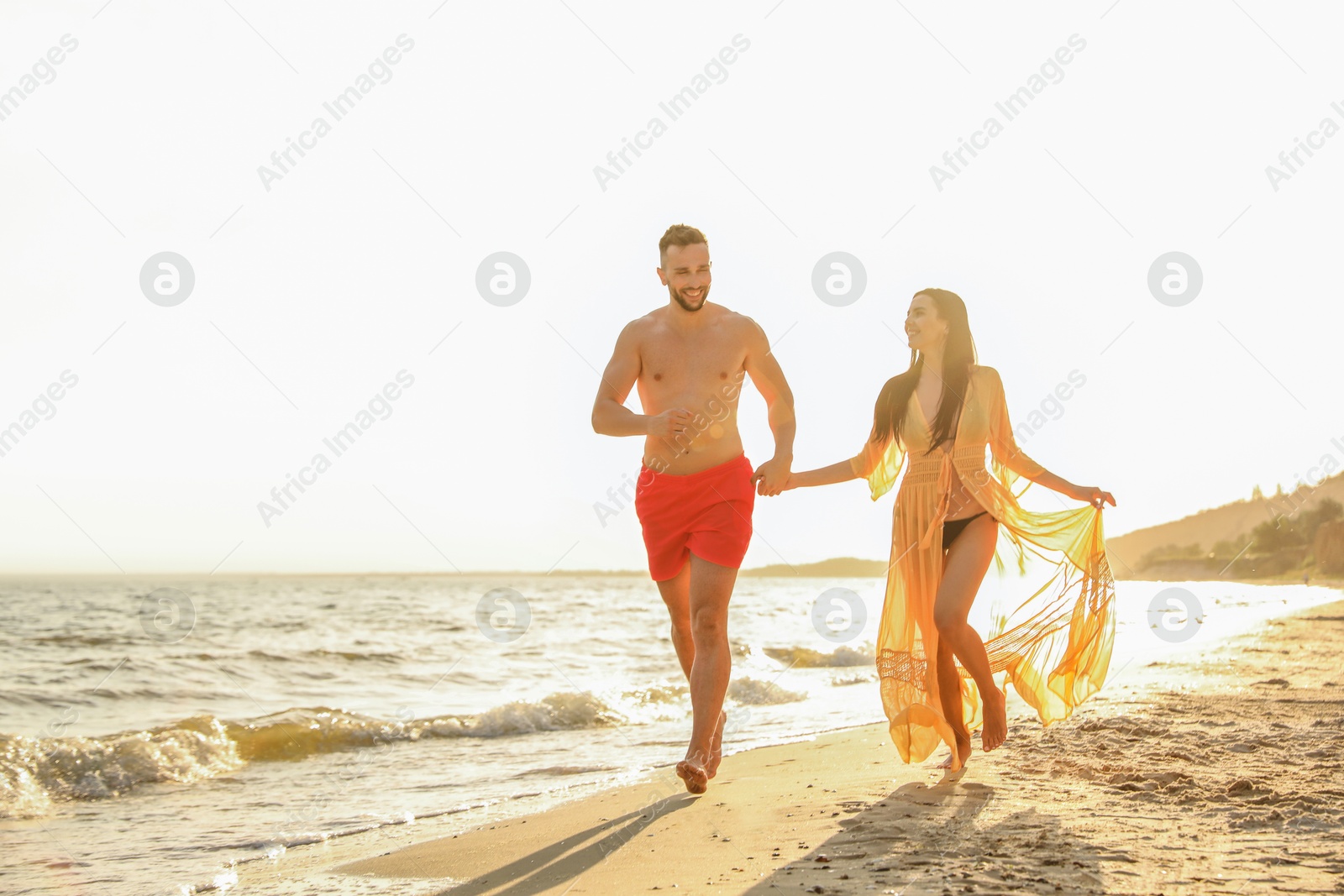 Photo of Happy young couple running together on beach at sunset