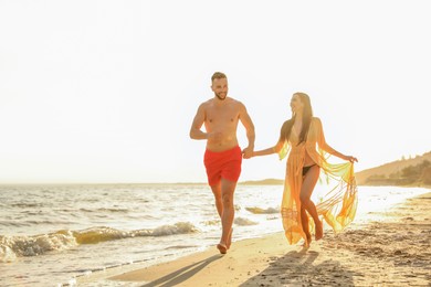 Photo of Happy young couple running together on beach at sunset