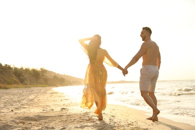 Photo of Happy couple walking together on beach at sunset, back view