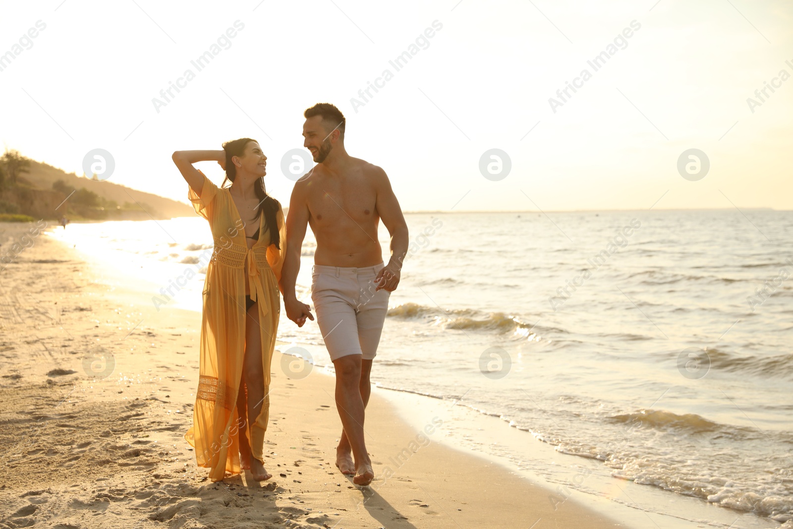 Photo of Happy young couple walking together on beach at sunset