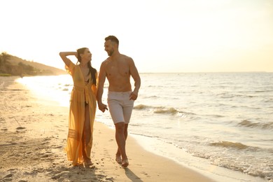 Photo of Happy young couple walking together on beach at sunset