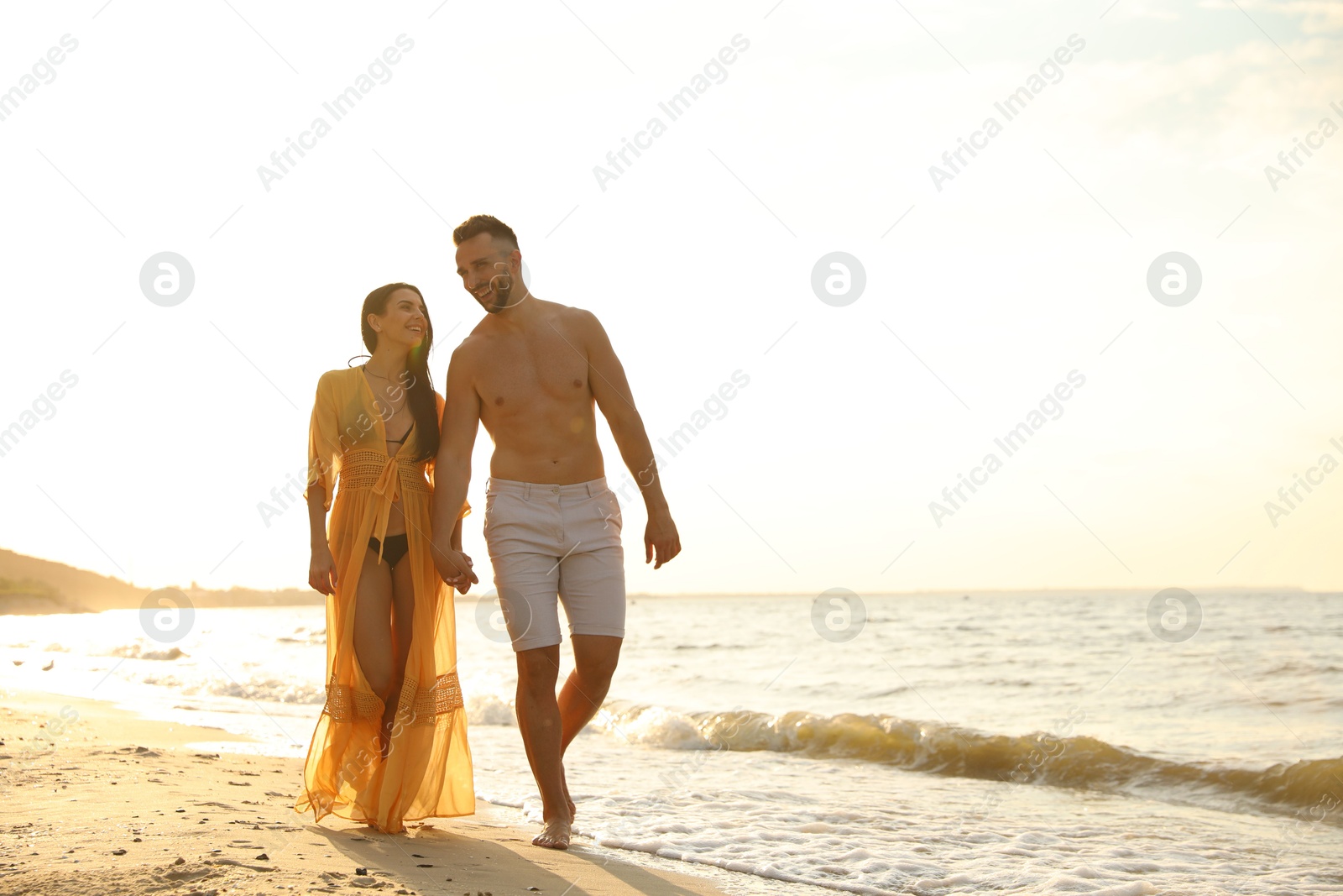 Photo of Happy young couple walking together on beach at sunset