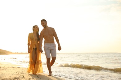 Photo of Happy young couple walking together on beach at sunset