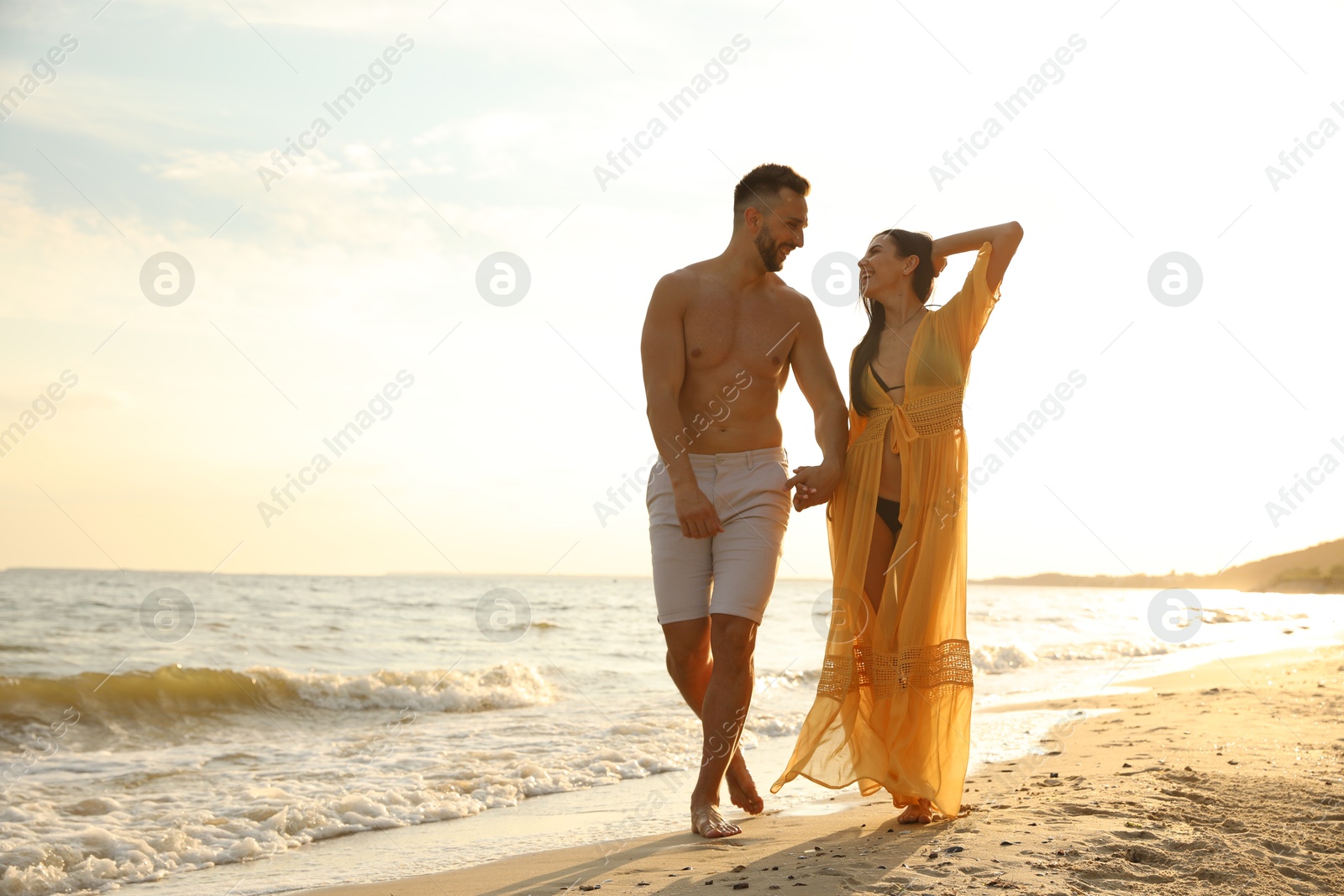 Photo of Happy young couple walking together on beach at sunset