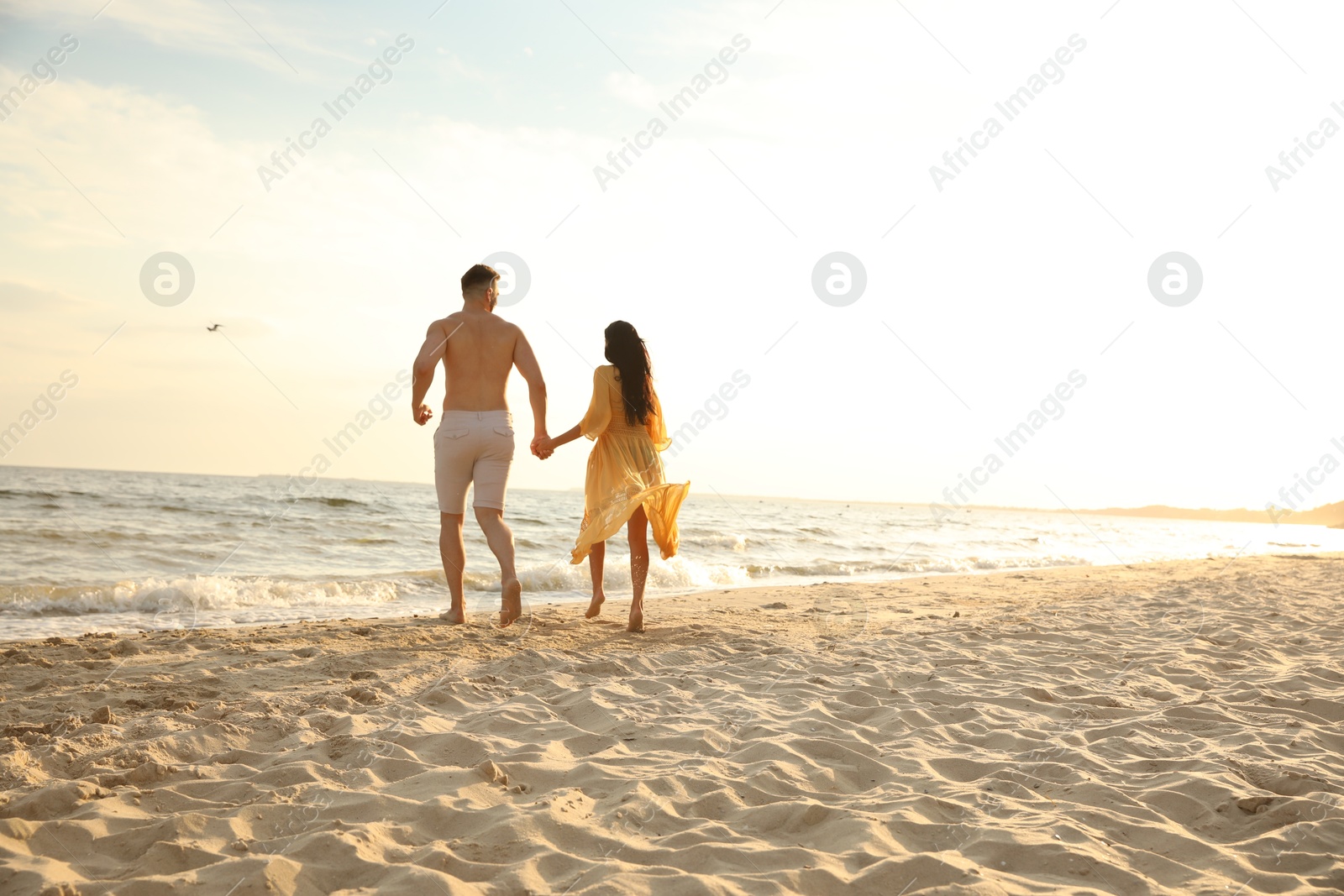 Photo of Lovely couple running together on beach at sunset, back view