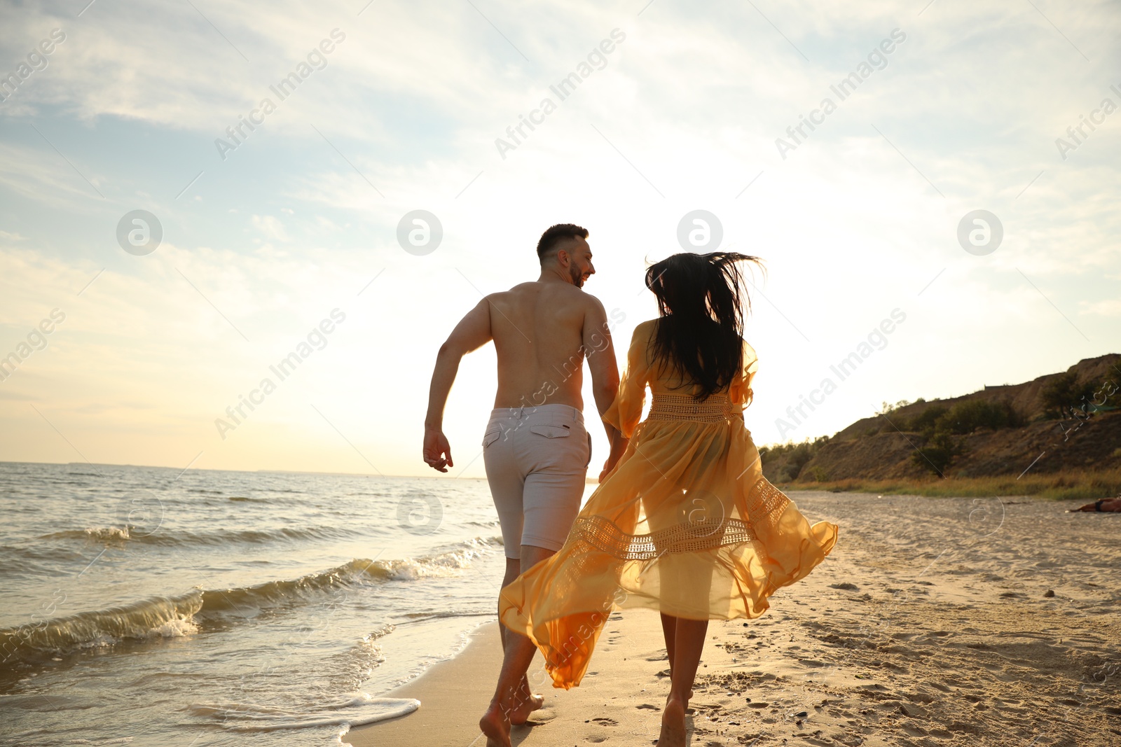 Photo of Lovely couple running together on beach at sunset, back view