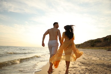 Photo of Lovely couple running together on beach at sunset, back view