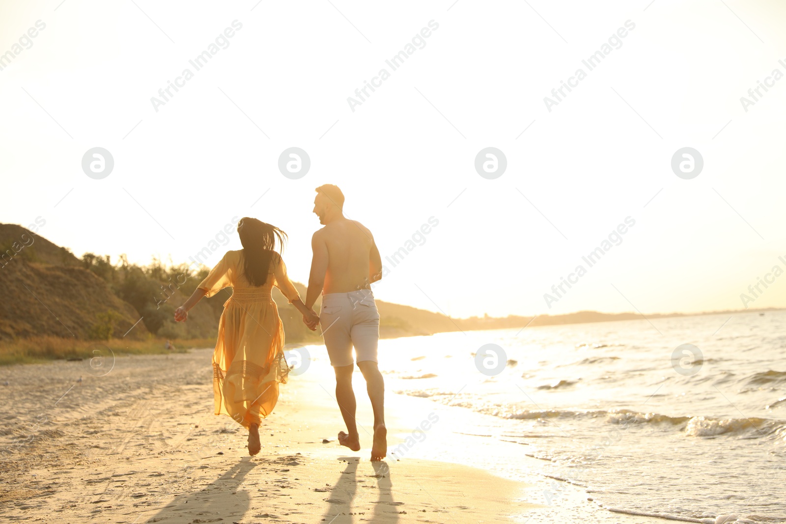 Photo of Lovely couple running together on beach at sunset, back view