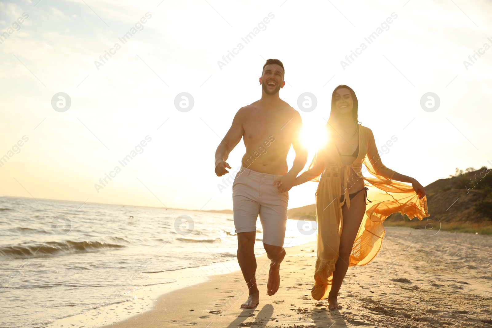 Photo of Happy young couple running together on beach at sunset