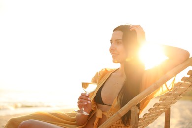 Photo of Young woman drinking wine on beach at sunset