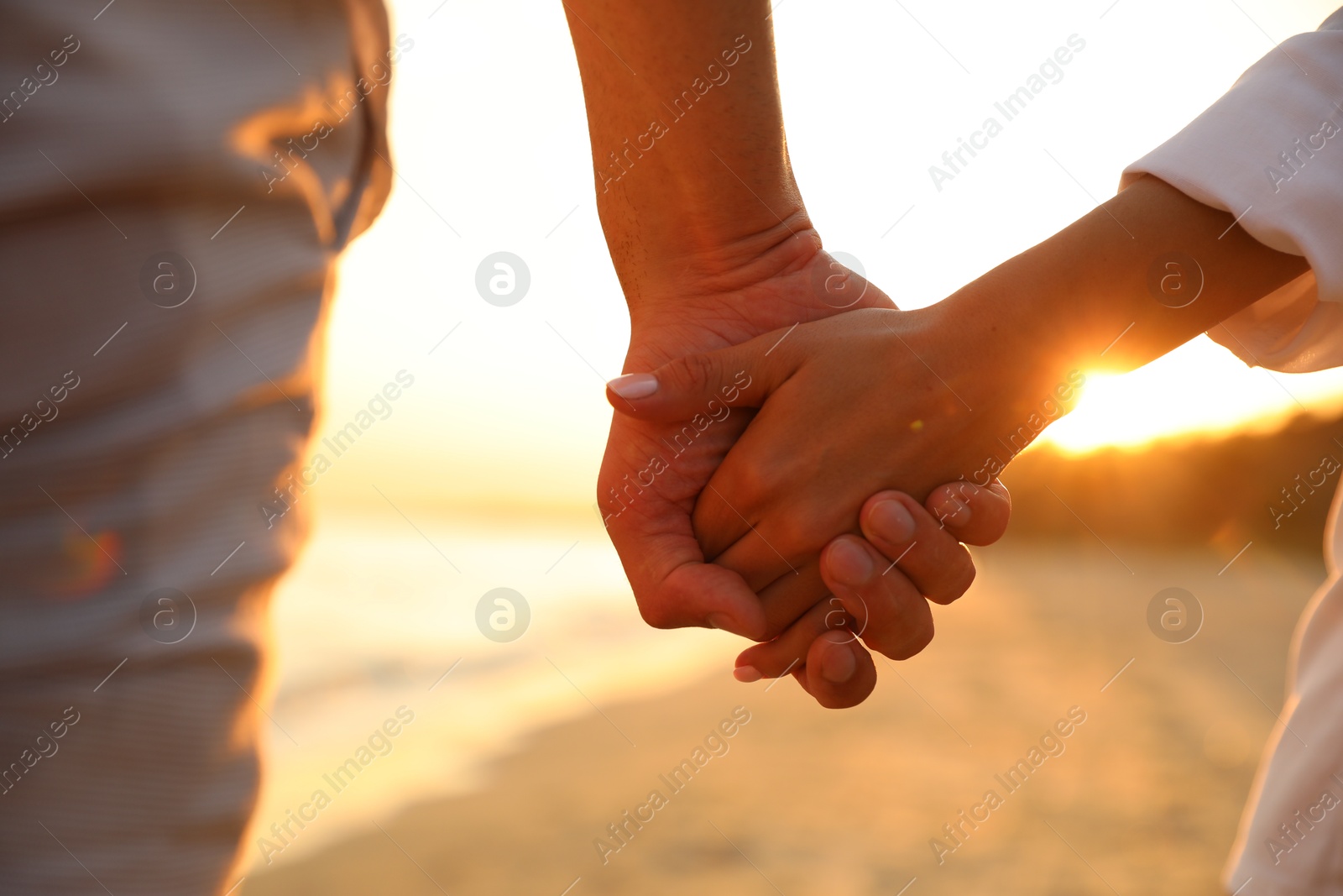 Photo of Lovely couple holding hands on beach at sunset, closeup