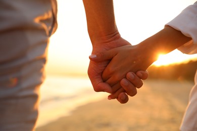 Photo of Lovely couple holding hands on beach at sunset, closeup