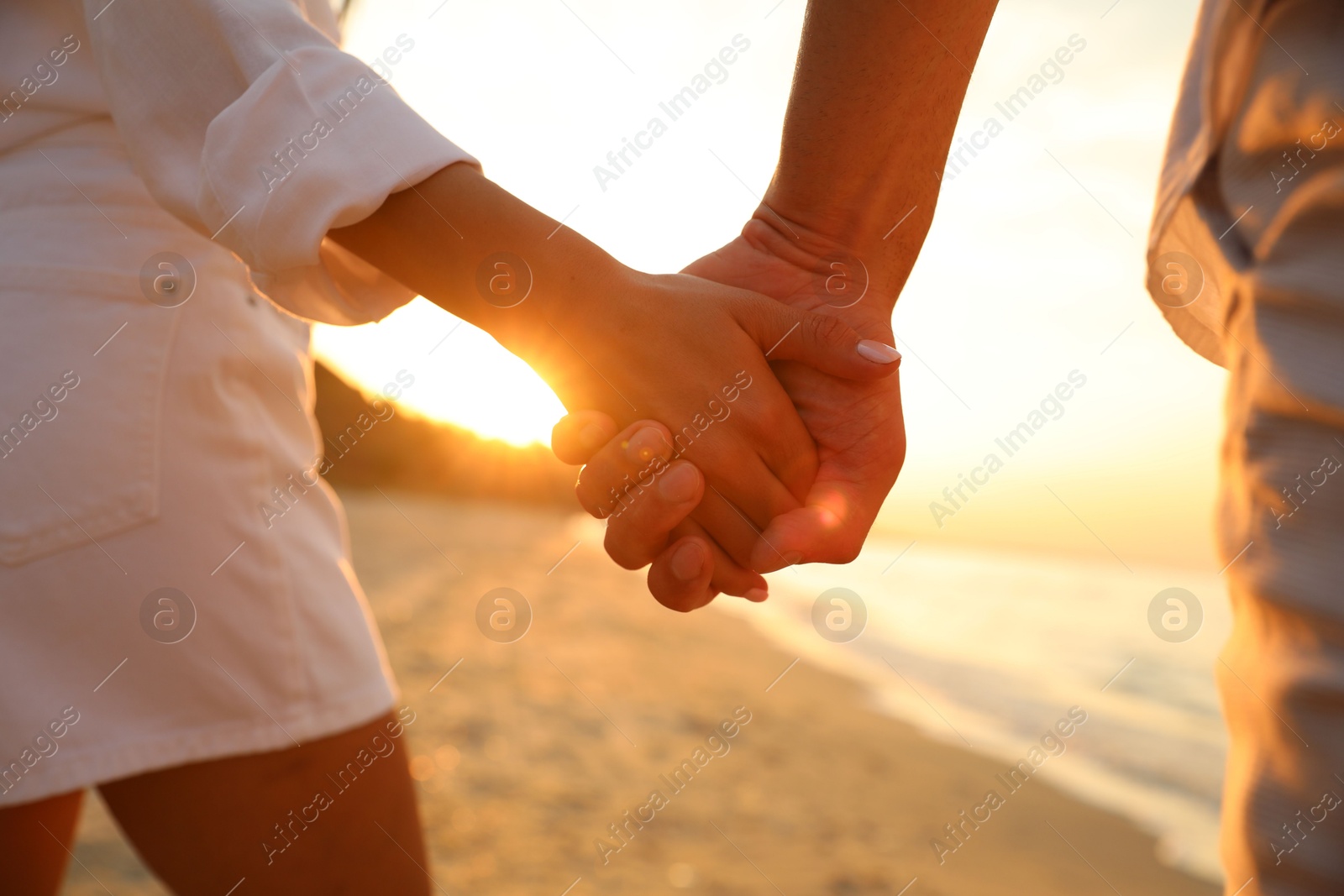 Photo of Lovely couple holding hands on beach at sunset, closeup