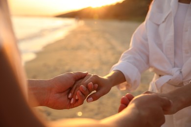 Photo of Lovely couple holding hands on beach at sunset, closeup