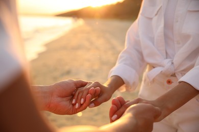 Photo of Lovely couple holding hands on beach at sunset, closeup