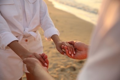 Photo of Lovely couple holding hands on beach at sunset, closeup