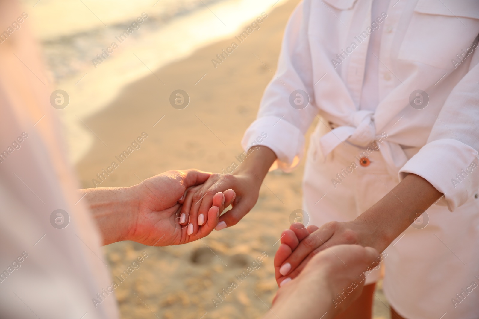 Photo of Lovely couple holding hands on beach at sunset, closeup