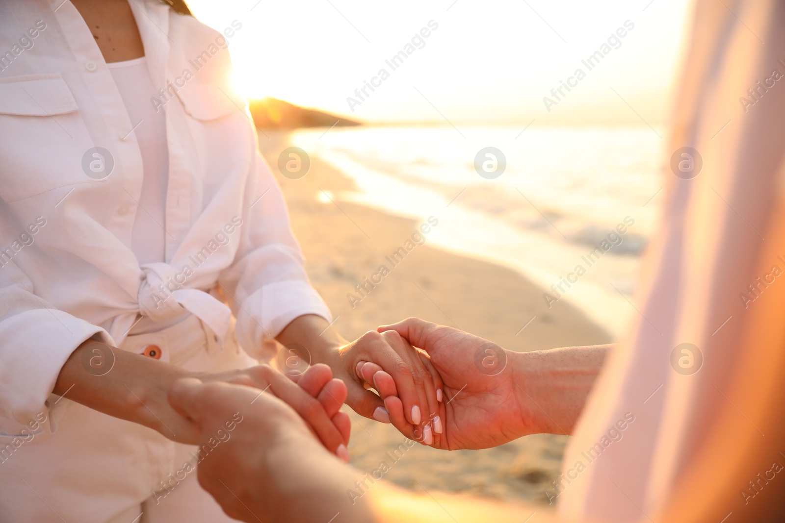 Photo of Lovely couple holding hands on beach at sunset, closeup