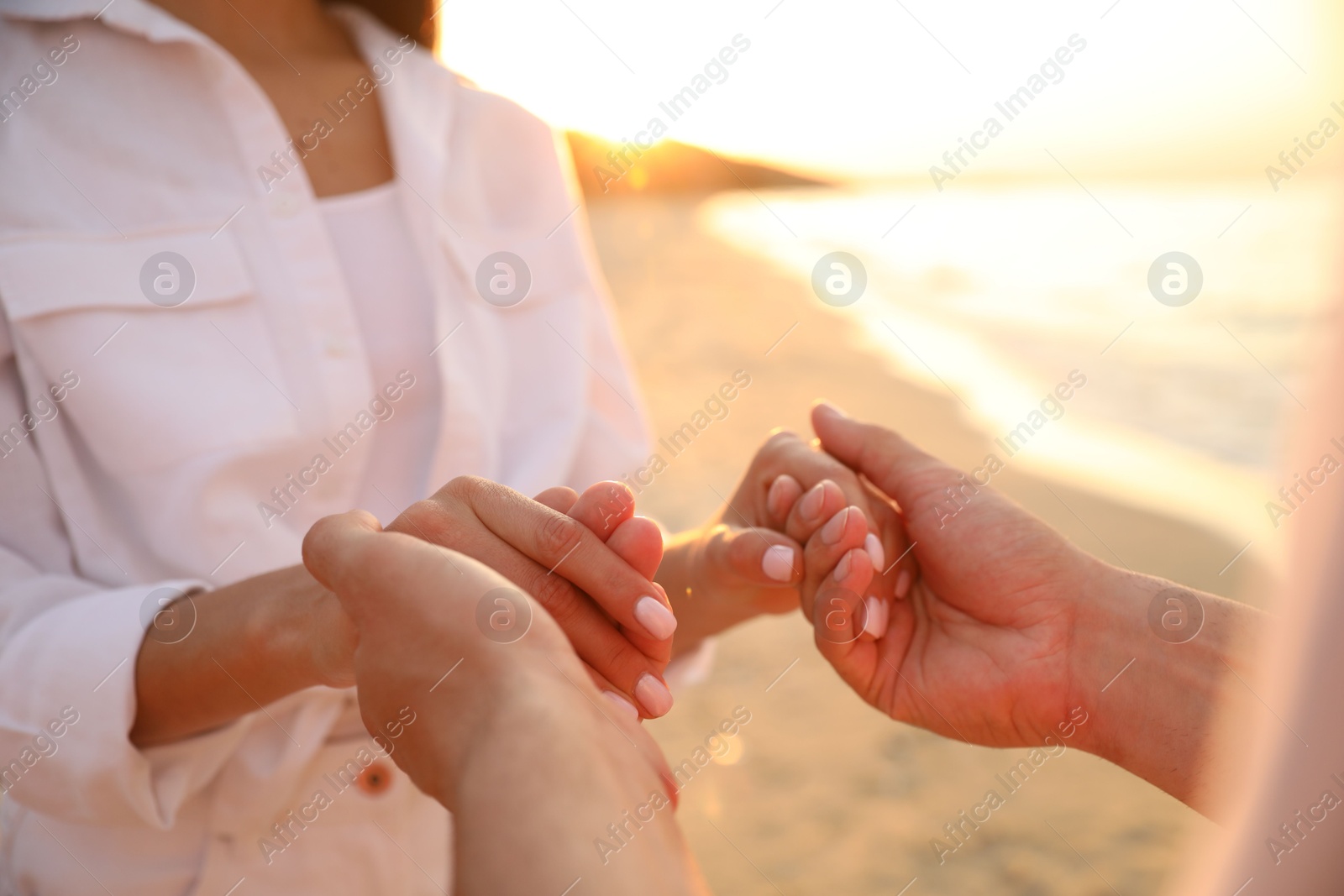 Photo of Lovely couple holding hands on beach at sunset, closeup