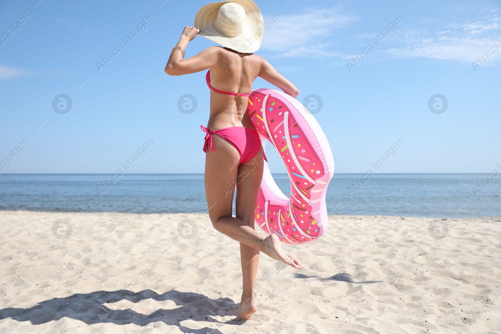 Photo of Young woman with beautiful body holding inflatable ring on sandy beach