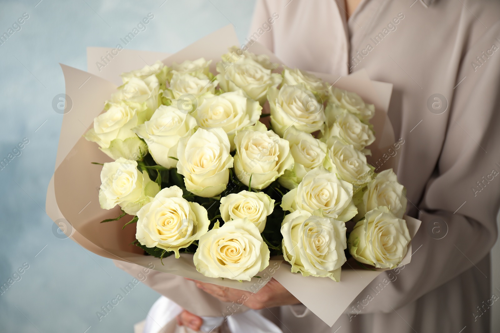 Photo of Woman holding luxury bouquet of fresh roses on light blue background, closeup