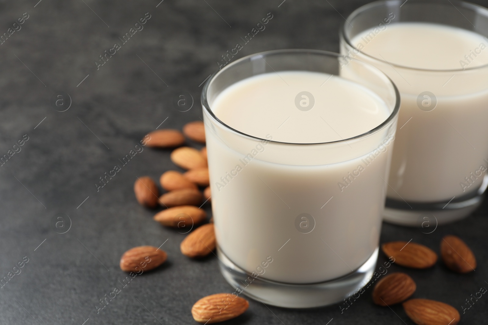 Photo of Fresh almond milk in glasses and nuts on dark grey table, closeup