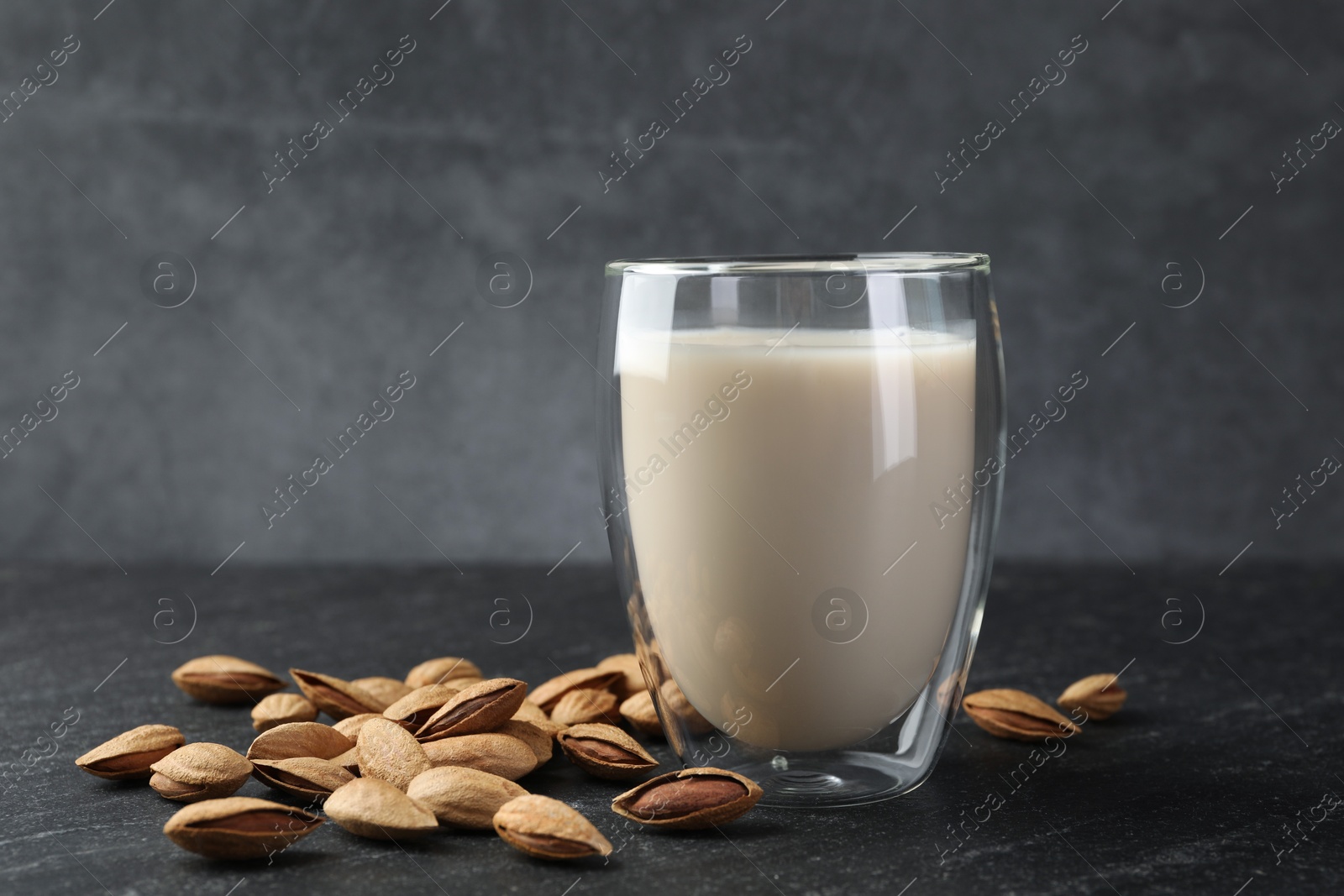 Photo of Fresh almond milk in glass and nuts on black table