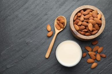 Photo of Fresh almond milk in glass, spoon and nuts on black table, top view. Space for text