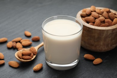 Photo of Fresh almond milk in glass, spoon and nuts on black table, closeup