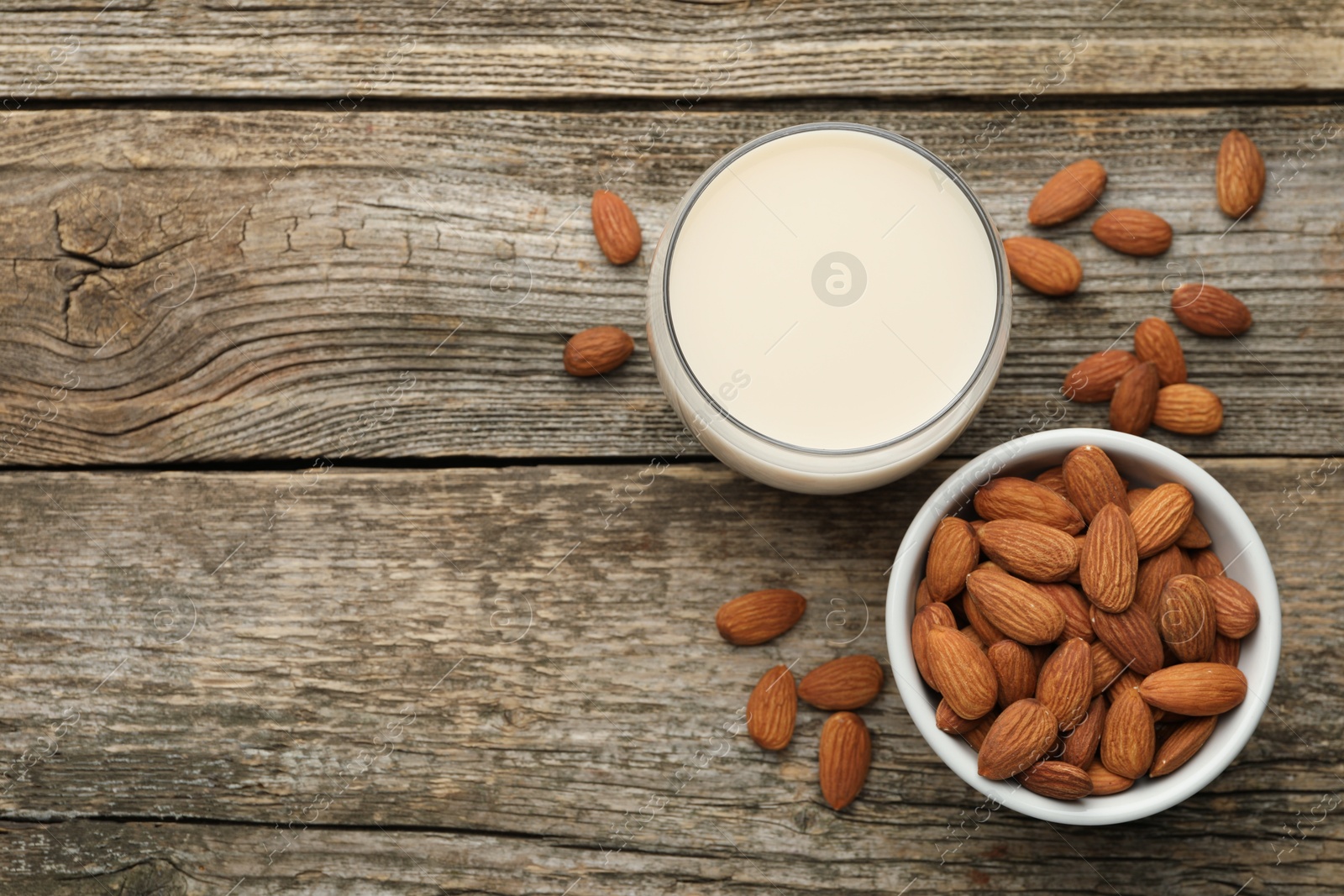 Photo of Fresh almond milk in glass and nuts on wooden table, top view. Space for text