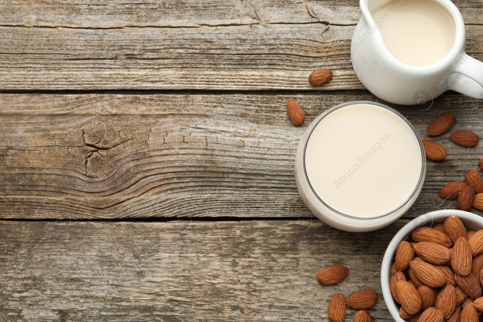 Photo of Fresh almond milk and nuts on wooden table, top view. Space for text