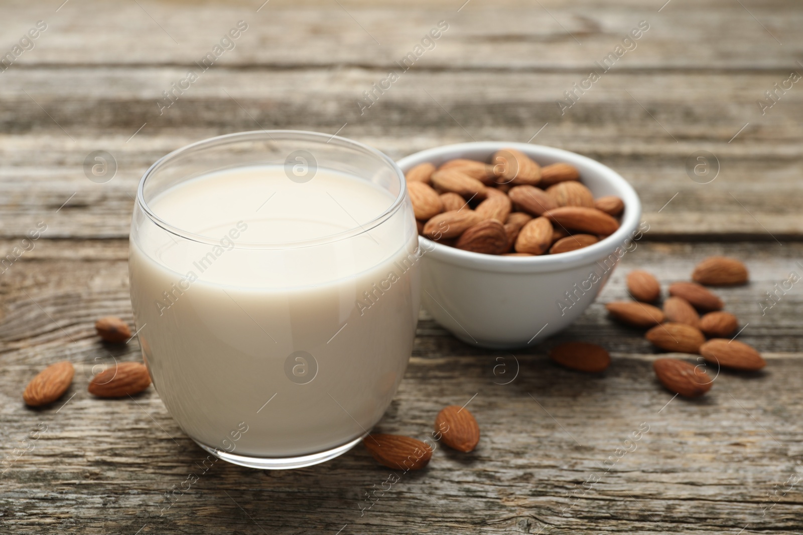 Photo of Fresh almond milk in glass and nuts on wooden table, closeup