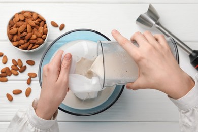 Photo of Woman making almond milk and nuts at white wooden table, top view