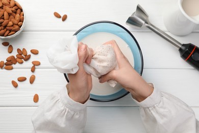 Photo of Woman making almond milk and nuts at white wooden table, top view