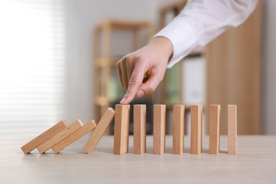 Photo of Woman stopping wooden blocks from falling at table, closeup. Domino effect