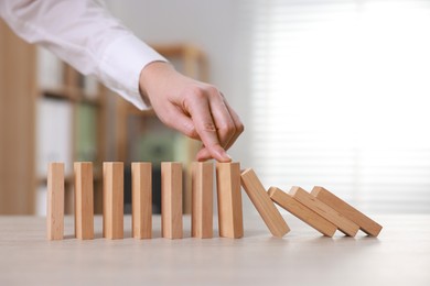 Photo of Woman stopping wooden blocks from falling at table, closeup. Domino effect