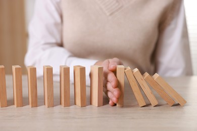 Photo of Woman stopping wooden blocks from falling at table, closeup. Domino effect